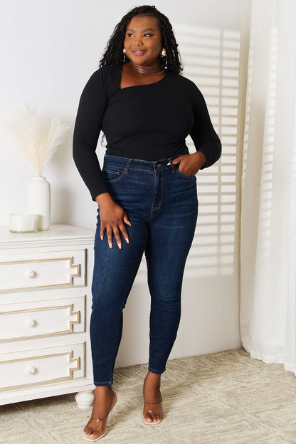 Woman wearing a black top and blue jeans standing in a room with white walls and a white dresser.