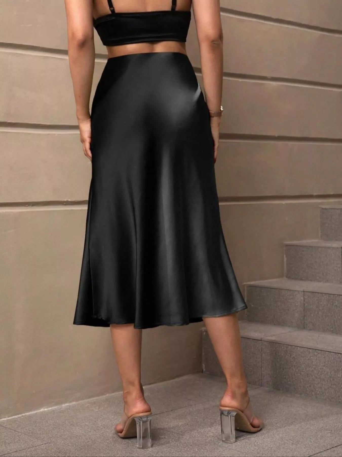 Person wearing a black satin skirt standing on steps with a neutral wall background