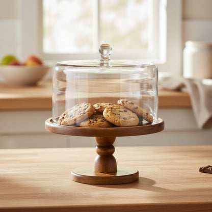 Wooden cake stand with a glass dome on a kitchen counter with cookies inside.