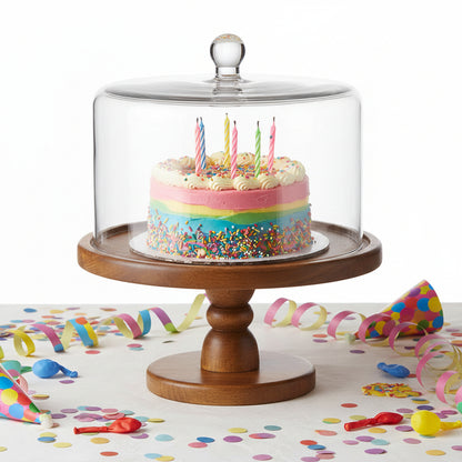 Wooden cake stand with a glass dome on a white background with a birthday cake inside.