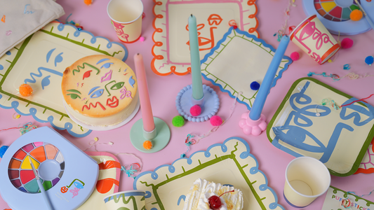 Colorful children's play area with art supplies, candles, and a cake on a pink surface.