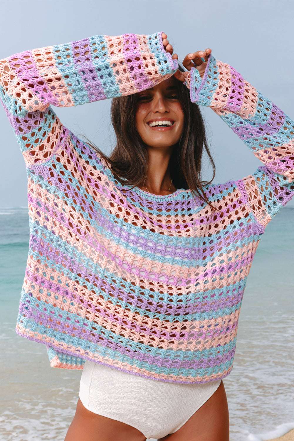 Pink, blue, and orange multi stripe open knit crochet sweater beach cover up worn by a woman at the beach.