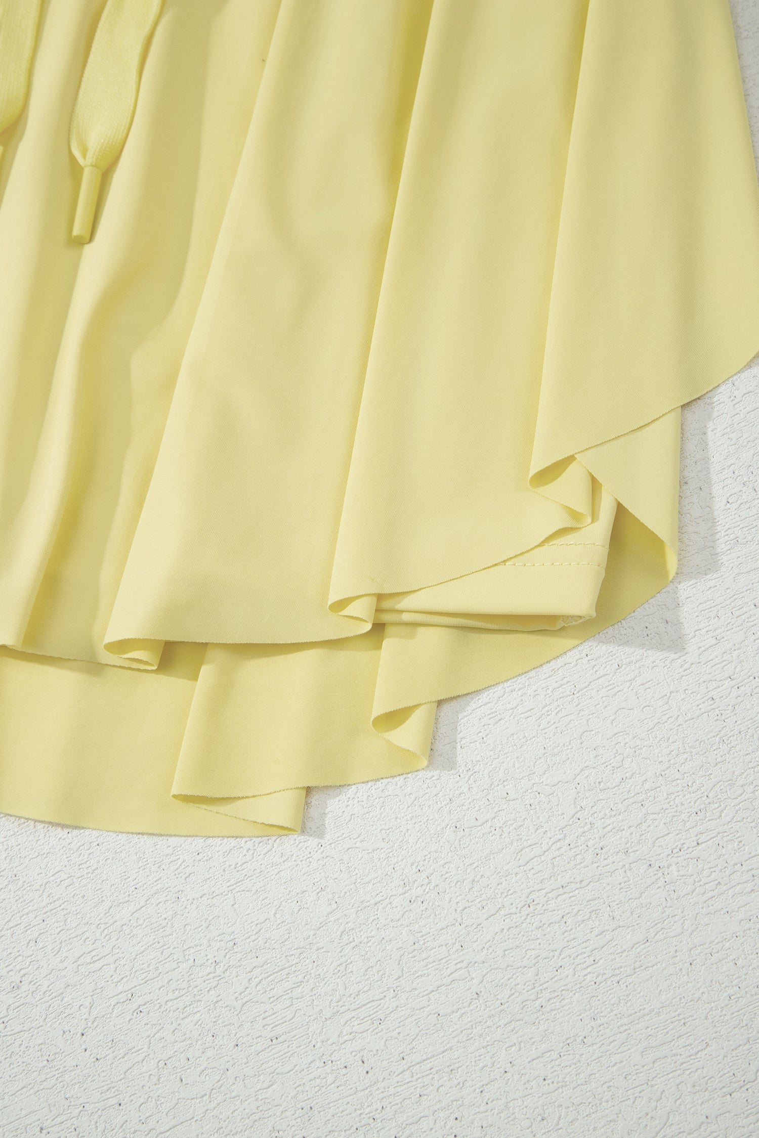 A close-up of a light pastel yellow draped fabric, showing soft folds and a textured white surface underneath.
