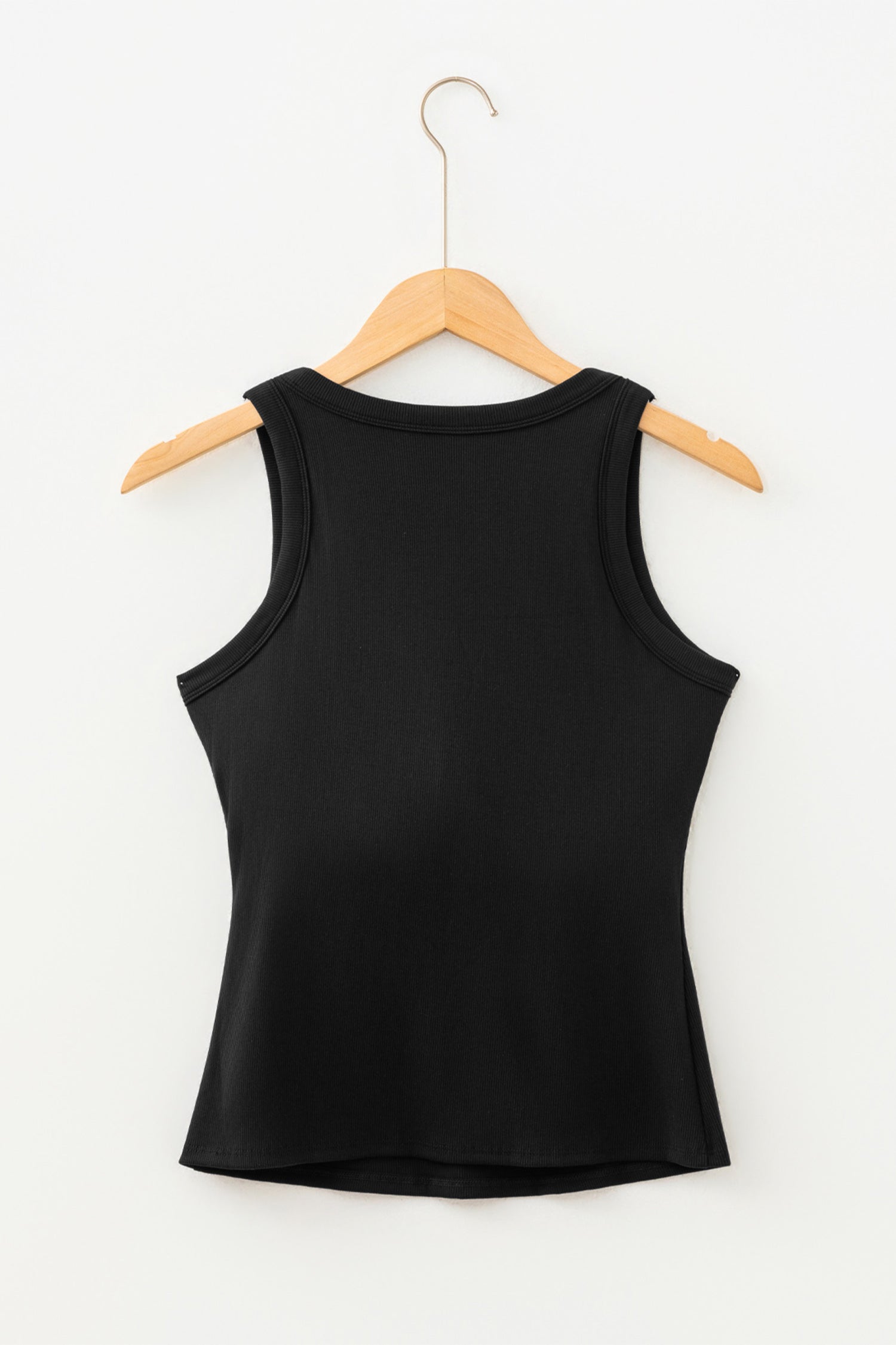 Black ribbed fabric tank top hanging on a light wood hanger against a white wall.