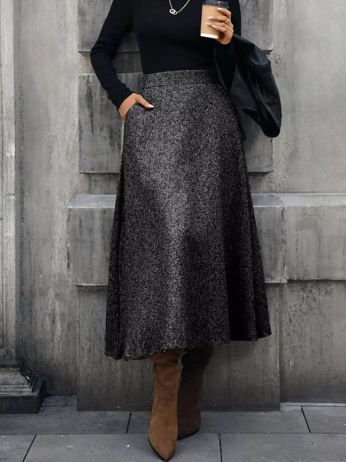 Person wearing a black top and gray skirt with brown boots against a gray wall.