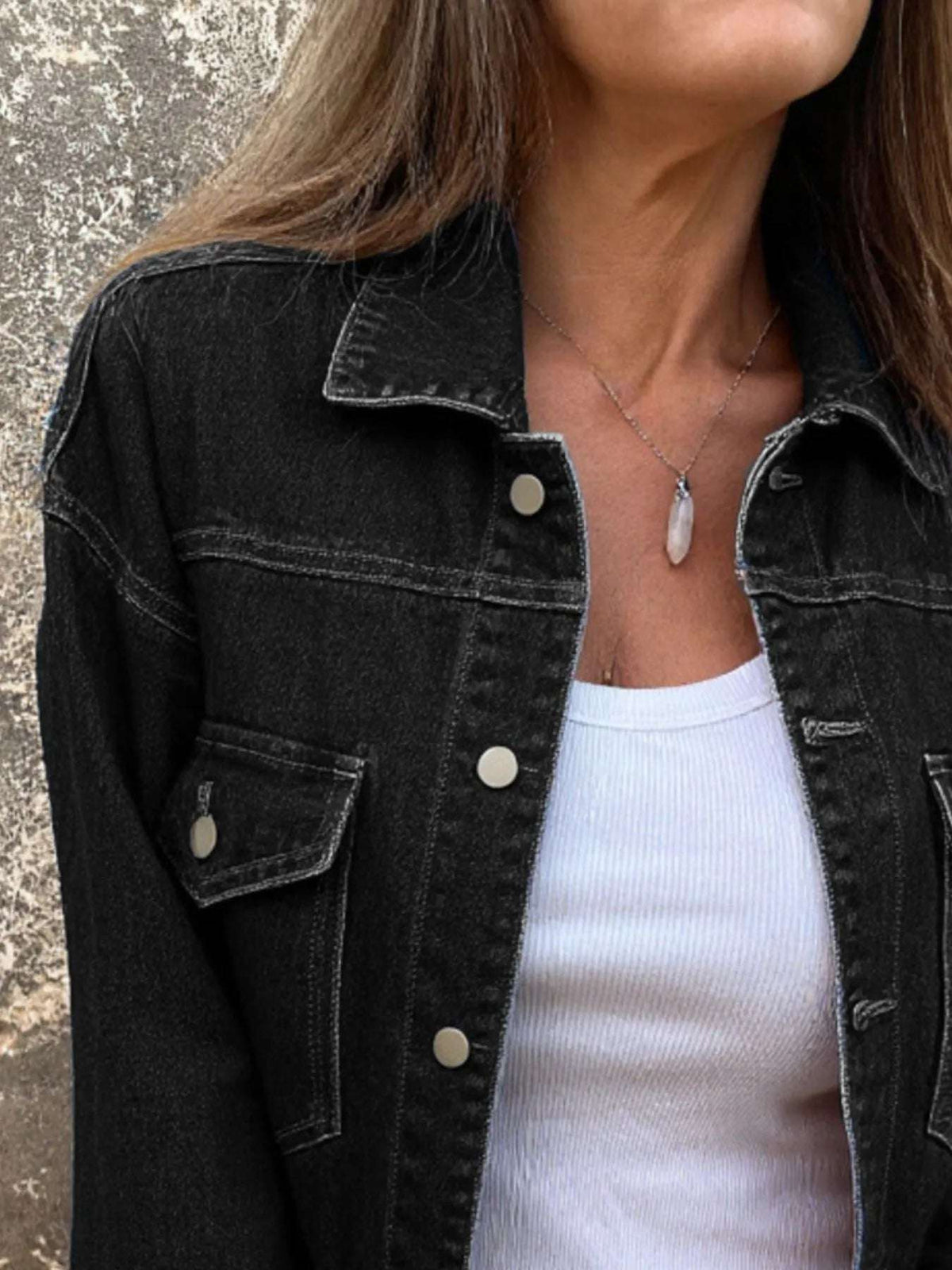 Person wearing a black denim jacket over a white top, with a neutral background