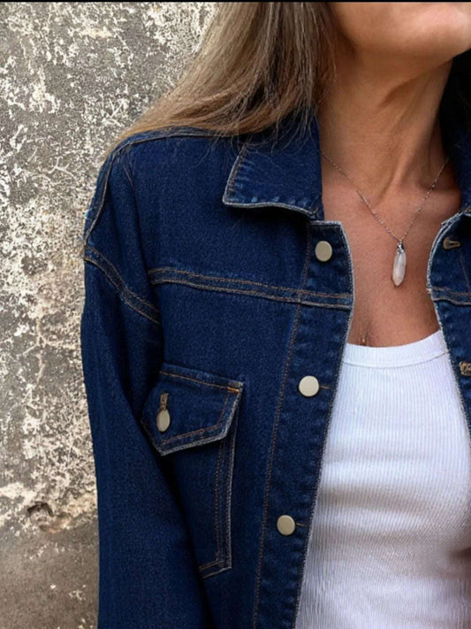Person wearing a blue denim jacket over a white top against a textured wall.