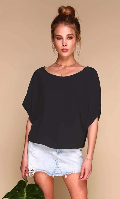 Woman wearing a black top and denim shorts against a beige background