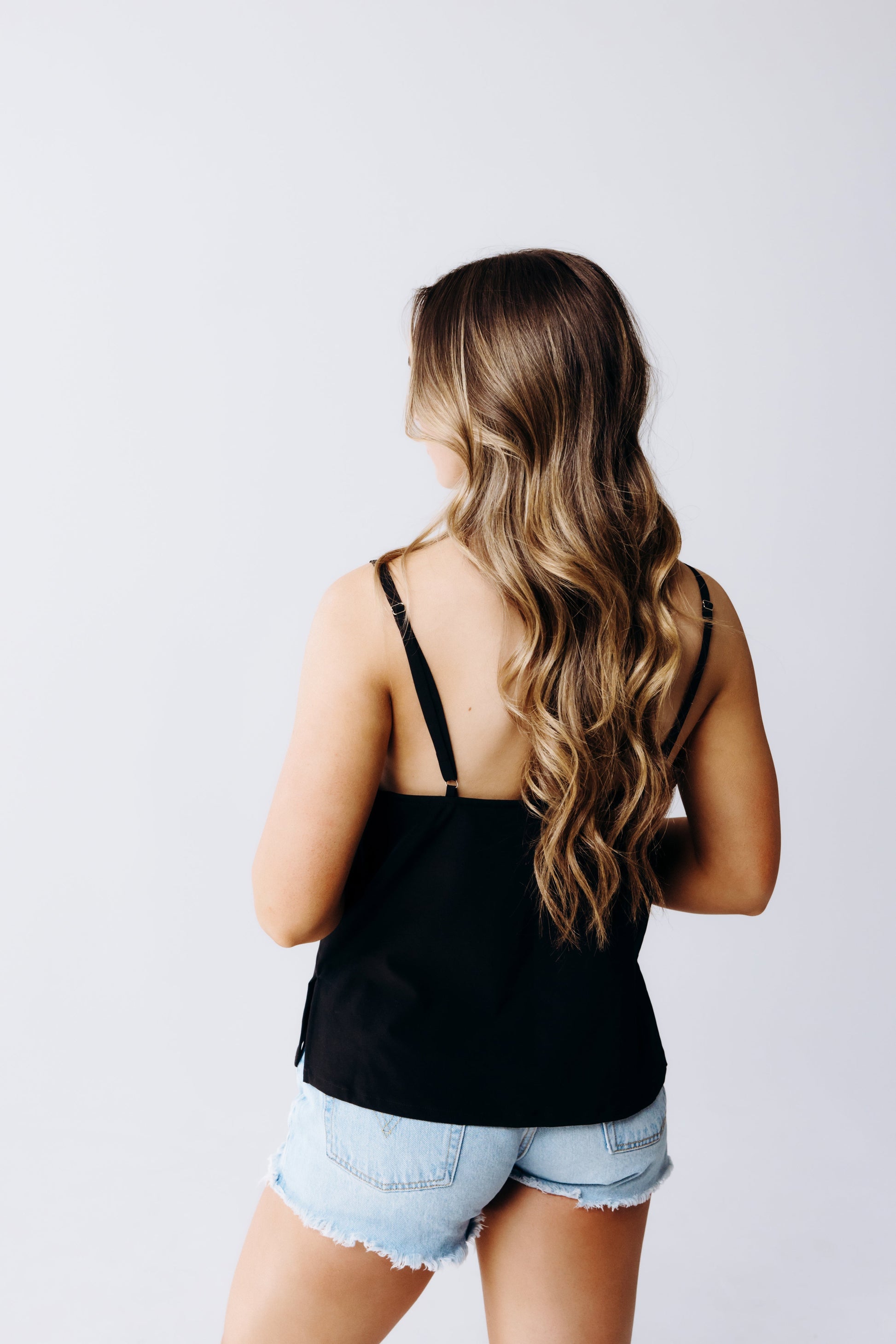 Woman wearing a black tank top and denim shorts on a white background