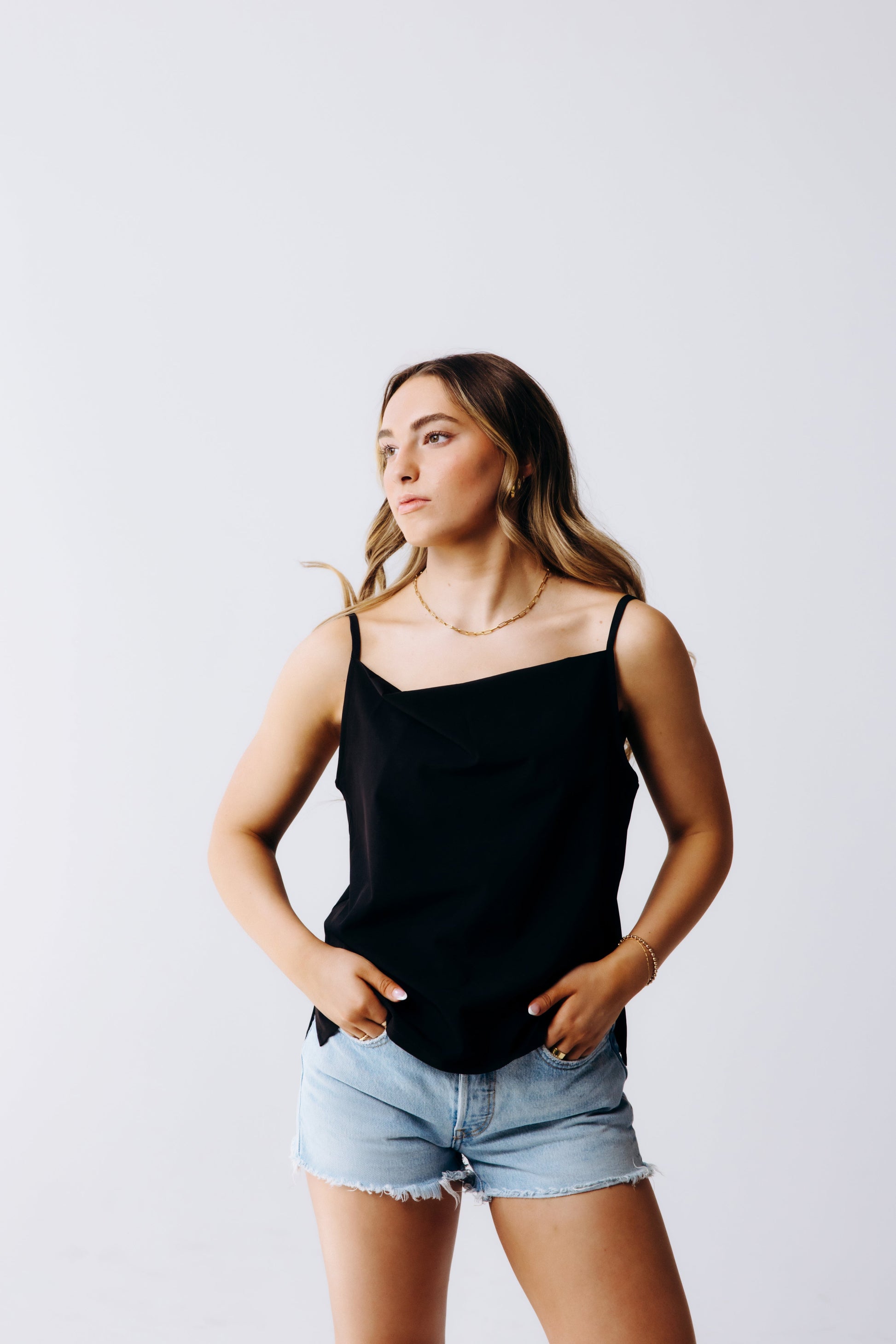 Woman wearing a black tank top and denim shorts against a plain background