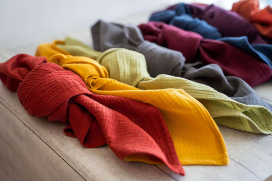 Knotted crinkle fabric napkins in red, yellow, green, grey, burgundy, and blue arranged on a light wood surface.