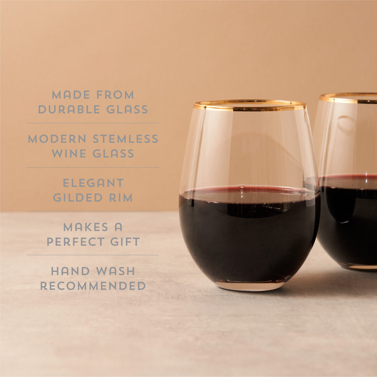 Two stemless wine glasses with gold rims filled with red wine on a beige background.