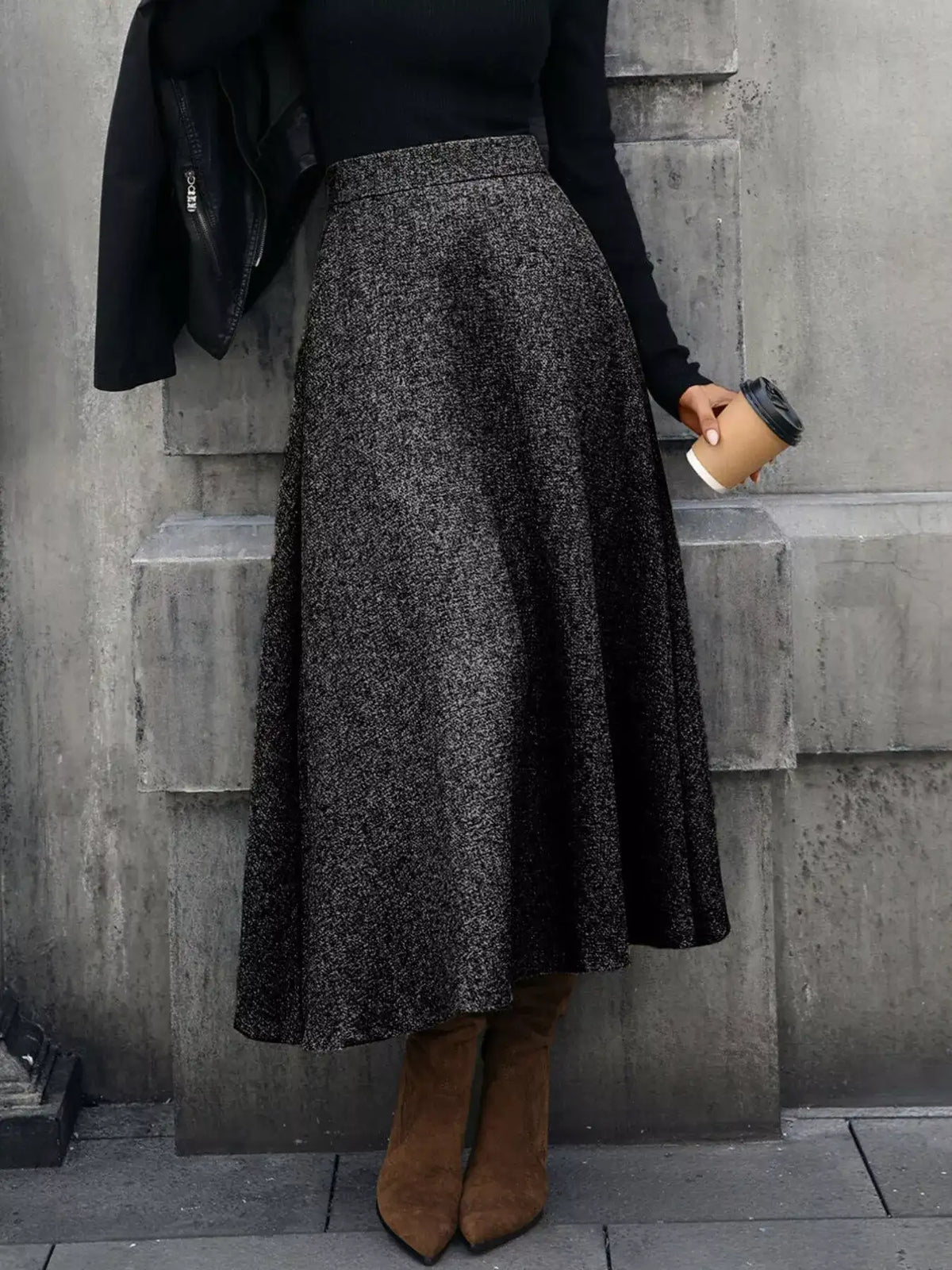 Person wearing a dark gray skirt and brown boots against a concrete wall.
