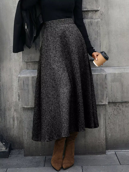 Person wearing a dark gray skirt and brown boots against a concrete wall.