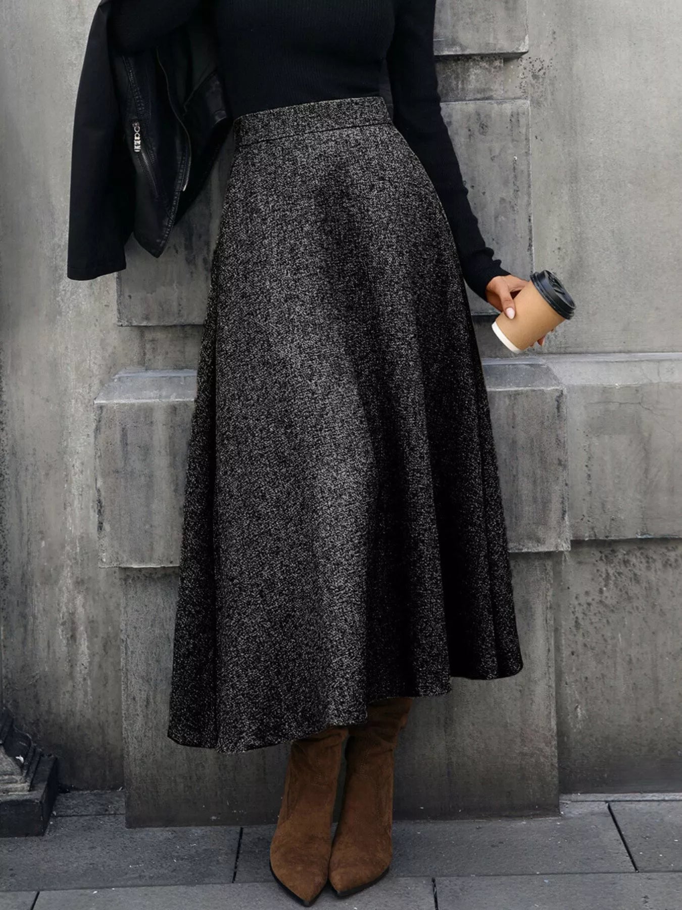 Person wearing a dark gray skirt and brown boots against a concrete wall.
