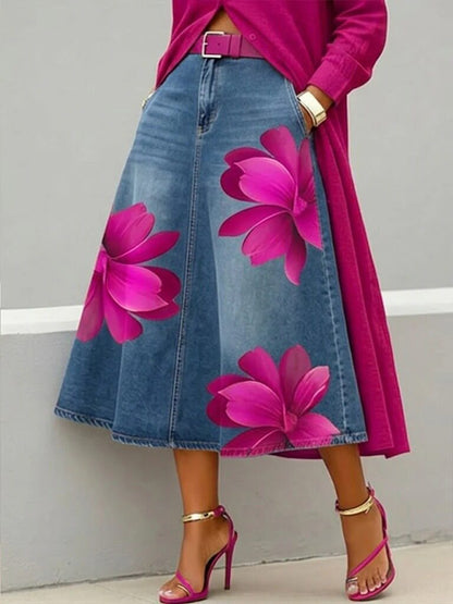Person wearing a pink floral dress with a blue denim skirt featuring pink flowers, standing against a gray background.
