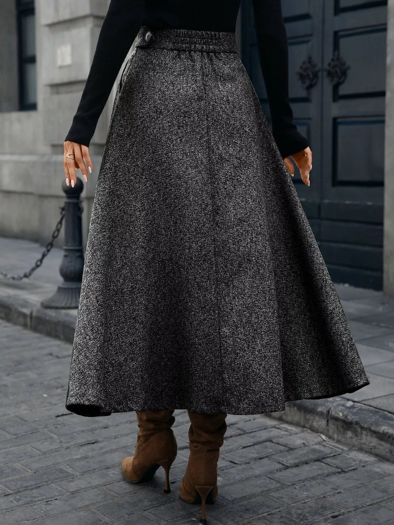 Person wearing a long gray skirt and brown boots on a city street.