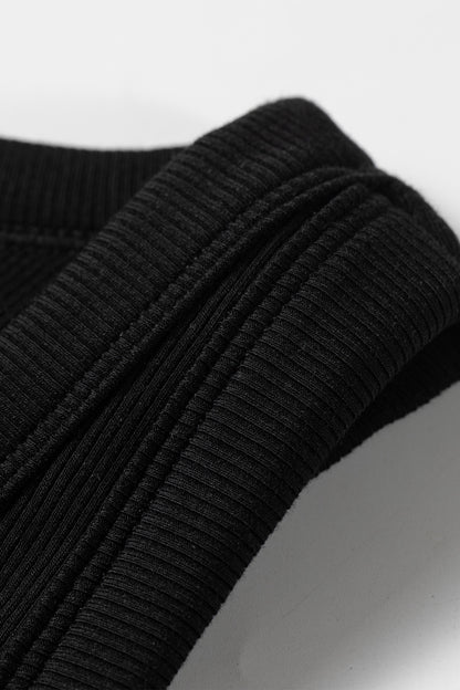 Close-up of a black ribbed sweater sleeve on a light gray background