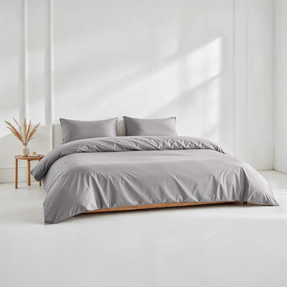 Gray bedding set on a bed in a minimalistic room with a white wall and wooden side table.