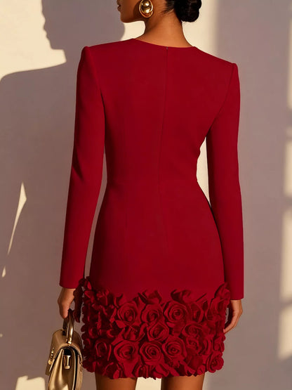 A woman shown from the back wearing a fitted long-sleeve red dress with a rose-patterned hem, holding a small metallic handbag against a sunlit beige wall.