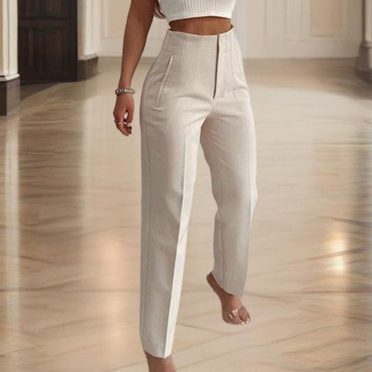 A model wearing a pair of high-waisted, off-white wide-leg trousers with a front zipper, walking on a polished wooden floor.