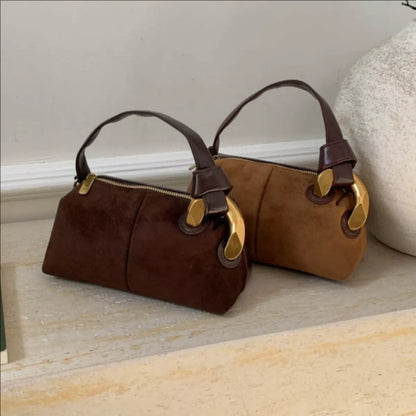 Two brown handbags with gold accents on a light wooden floor.