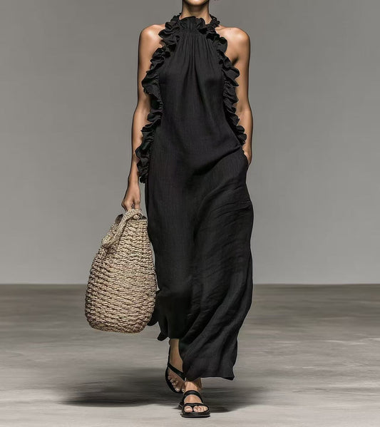 Woman wearing a black dress with ruffled neckline and holding a woven bag on a gray background