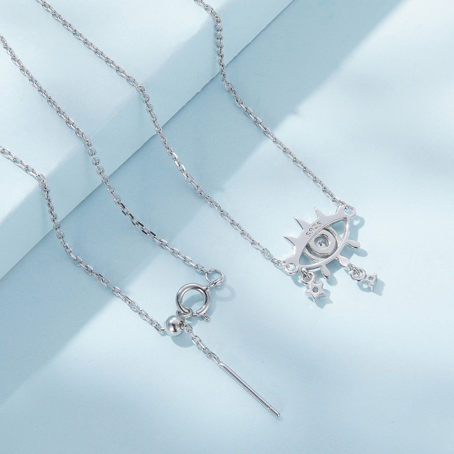 Back view of two silver necklaces with charms on a light blue background