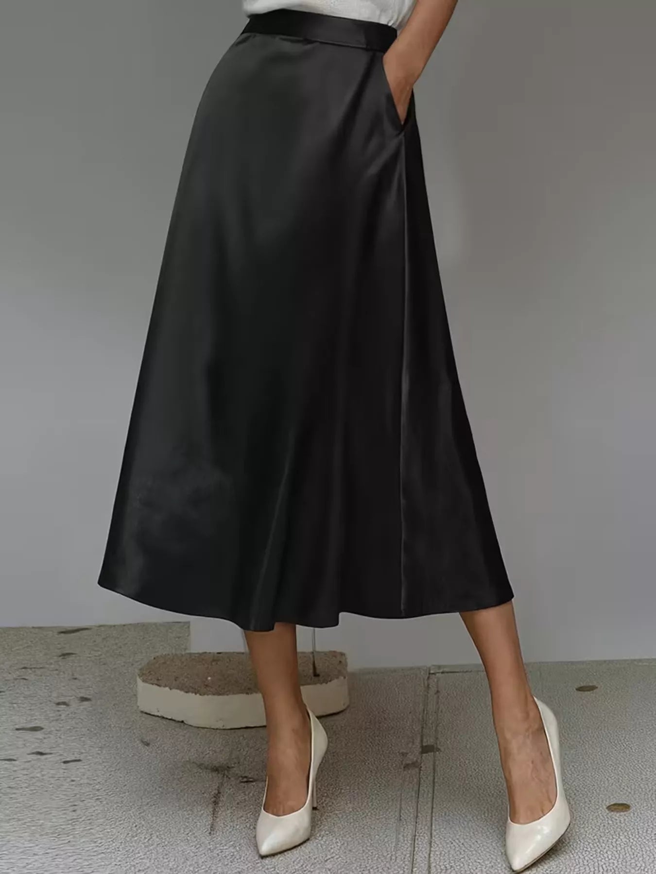 Person wearing a black satin skirt with white shoes on a neutral background