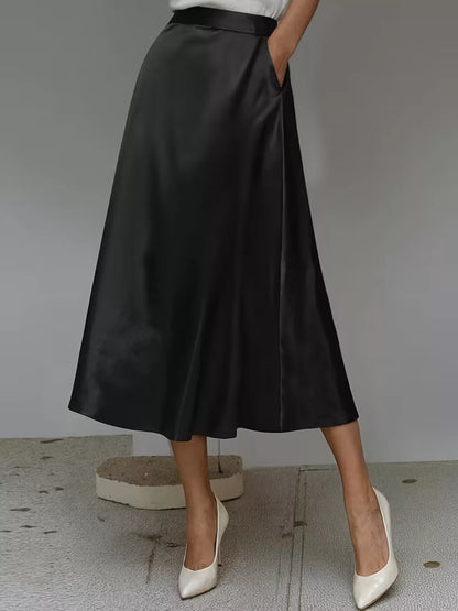 Person wearing a black satin skirt with white shoes on a neutral background