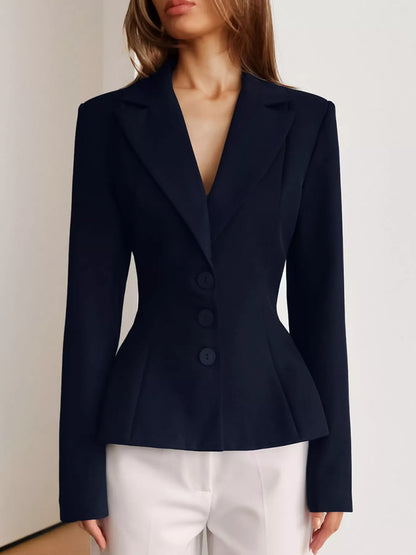 A woman wearing a tailored navy blazer with structured shoulders, a deep V-neckline, and three front buttons, paired with white pants against a plain light background.