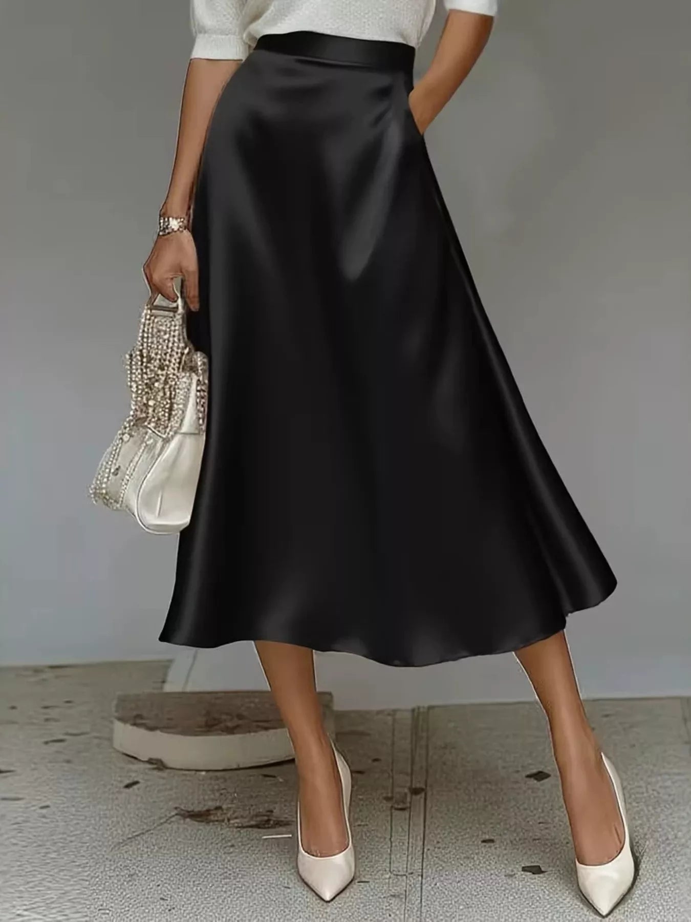Person wearing a black satin skirt with white shoes and a decorative handbag.