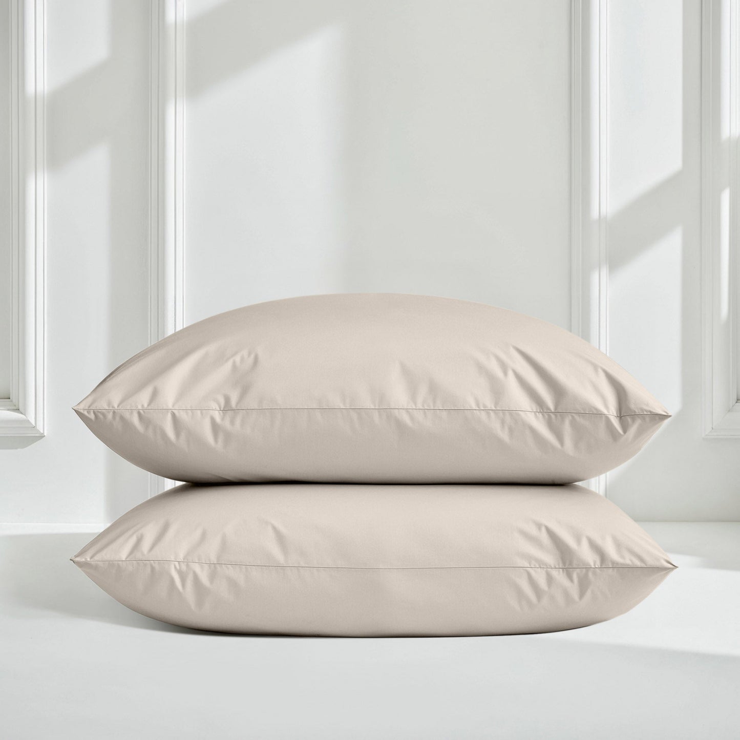 Two beige pillows on a light gray surface with a white paneled wall background