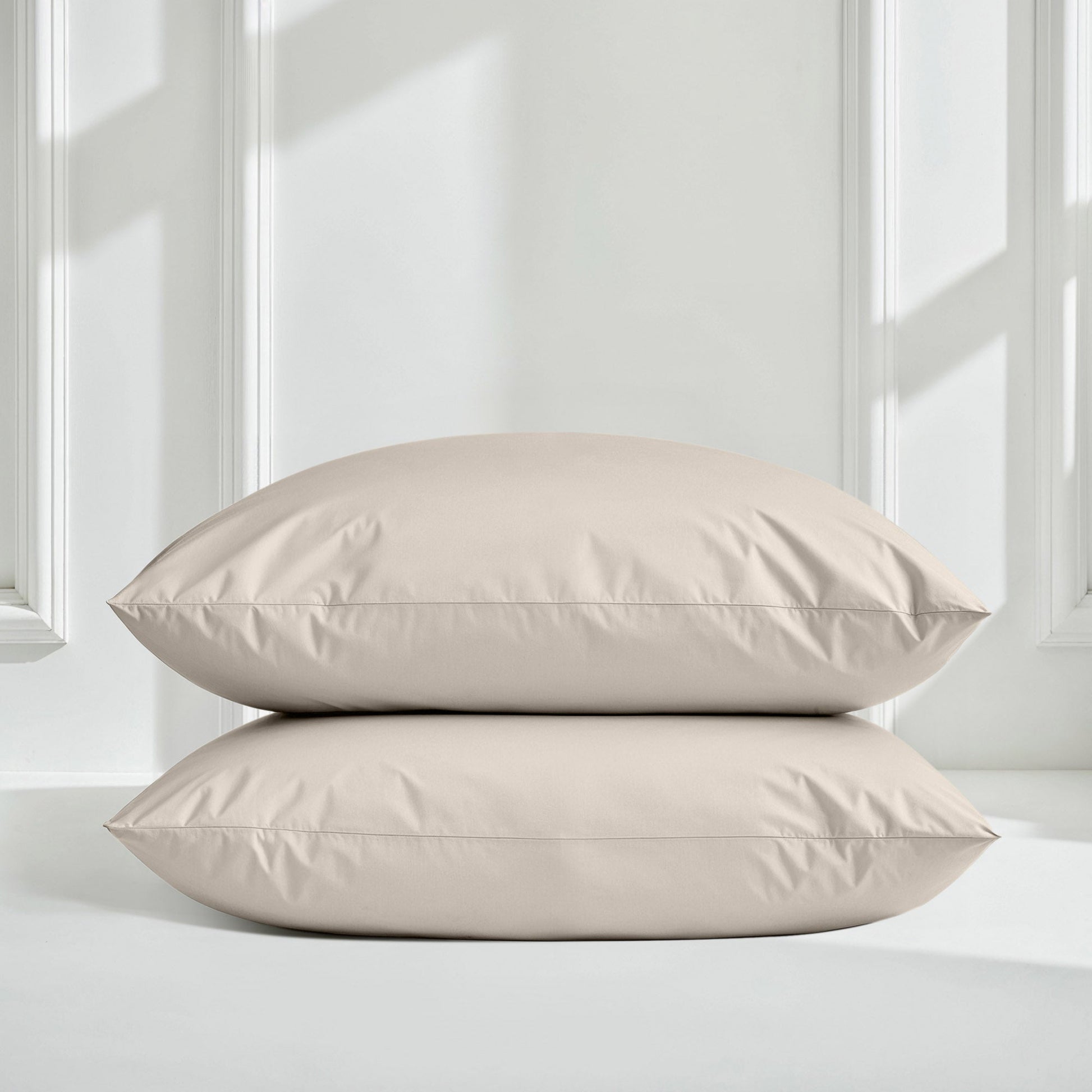 Two beige pillows on a light gray surface with a white paneled wall background