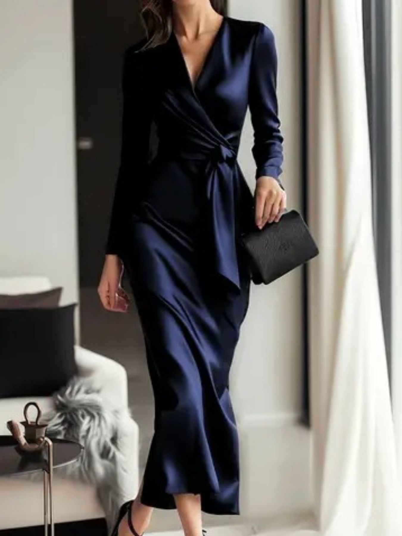 Woman in a navy blue dress holding a black clutch in an indoor setting.