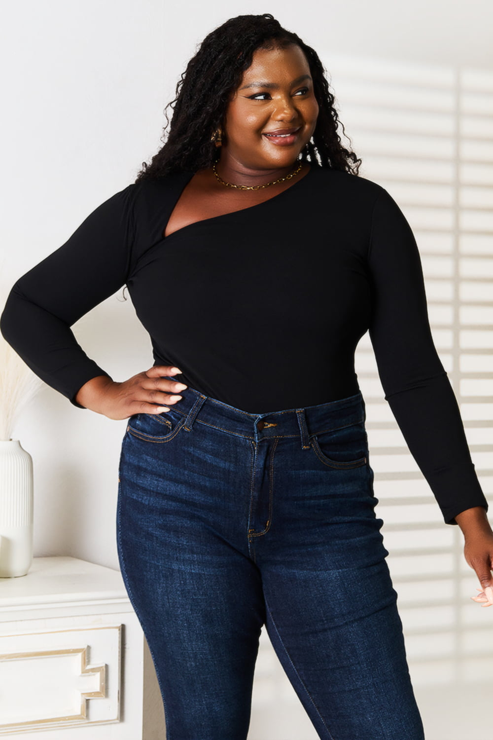 Woman wearing a black long-sleeve top and blue jeans indoors.