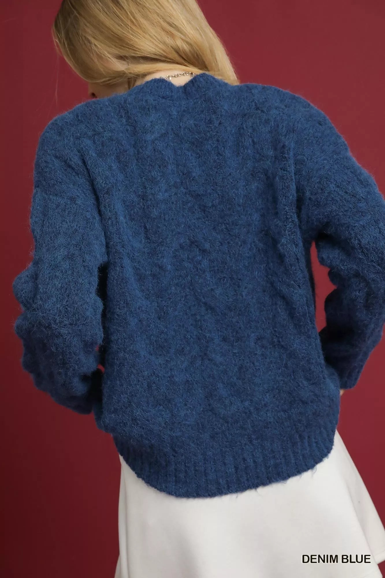 Young woman wearing a blue cable knit sweater.