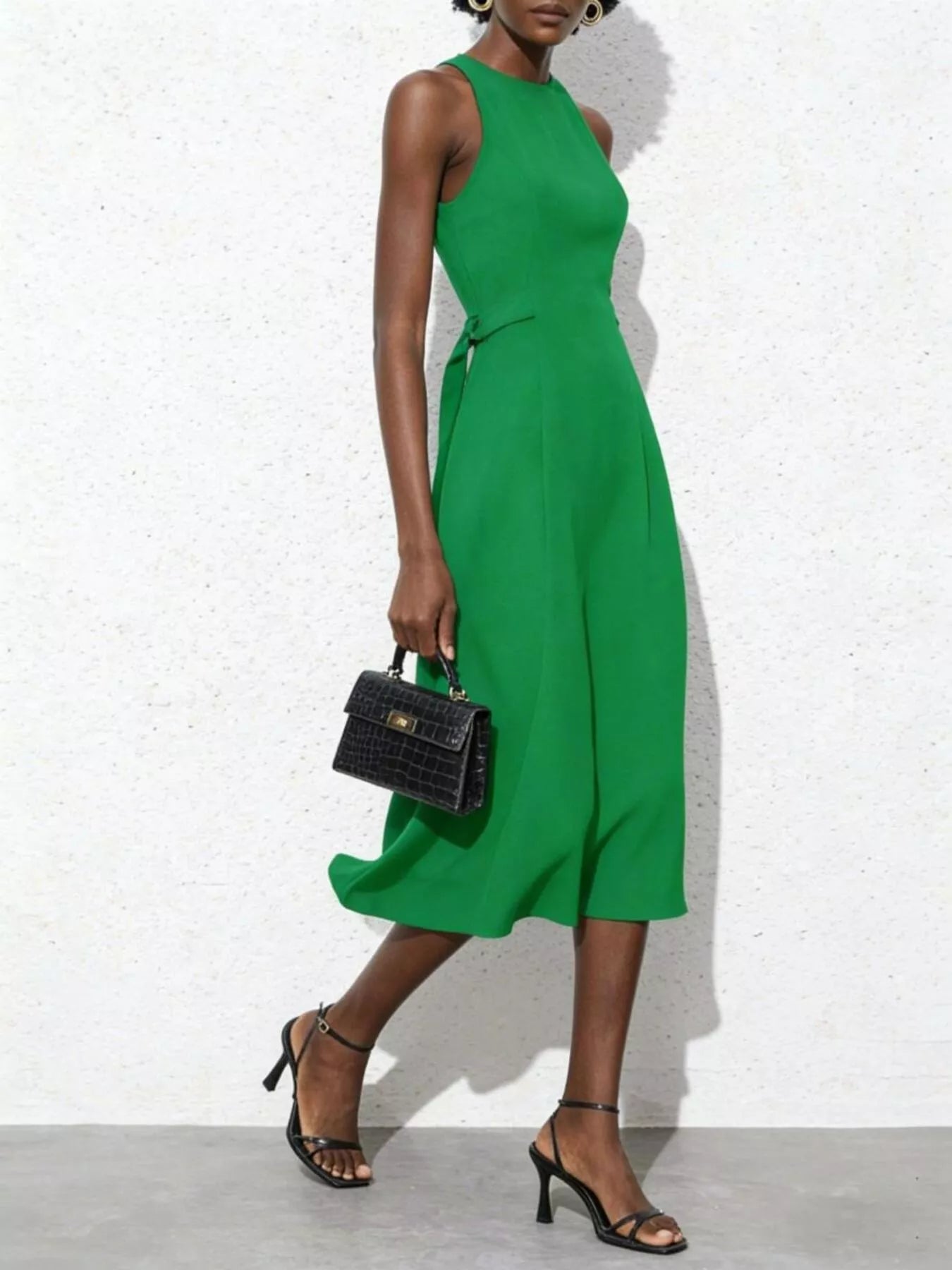 Woman wearing a green dress holding a black handbag against a white background