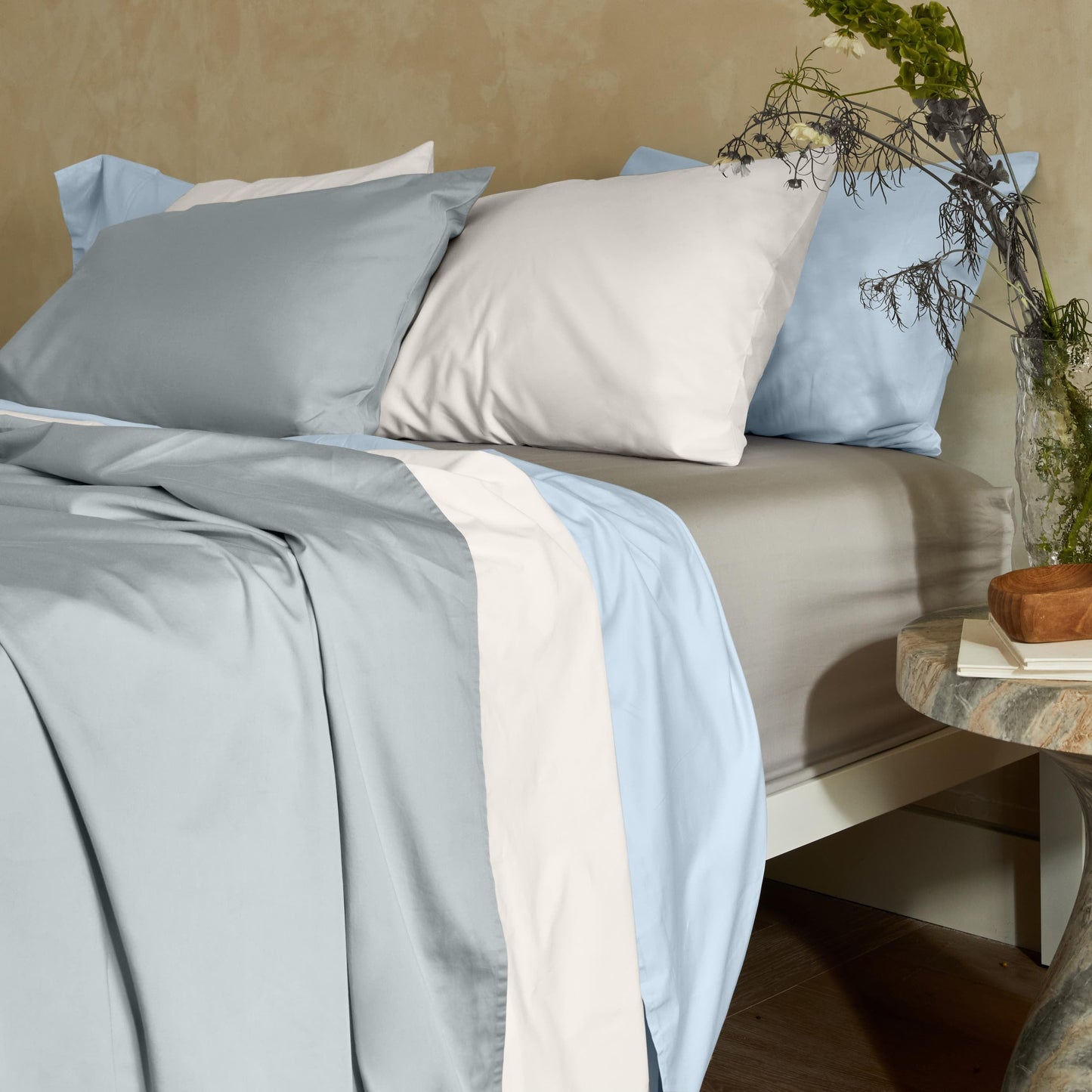 Bed with light blue and white bedding, pillows, and a side table with decor items.