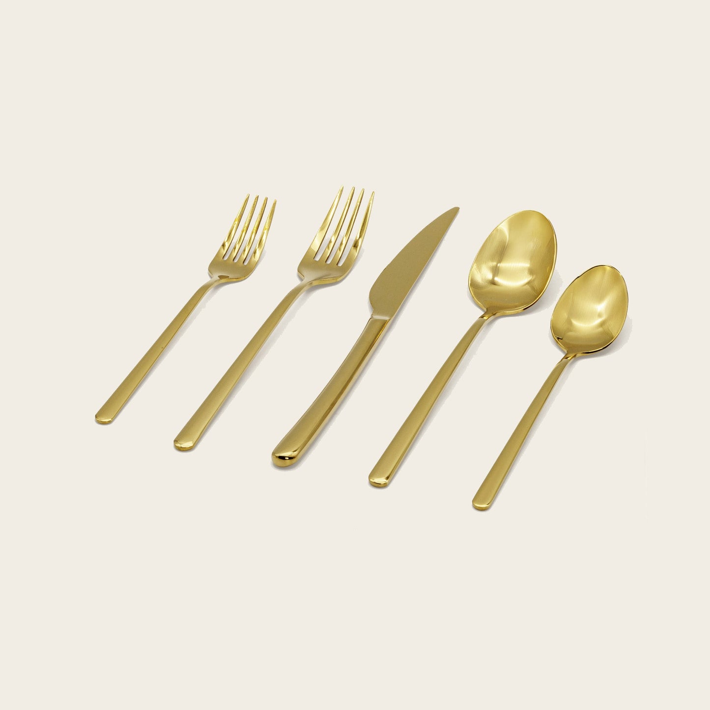 Set of gold cutlery including forks, a knife, and spoons on a light beige background.