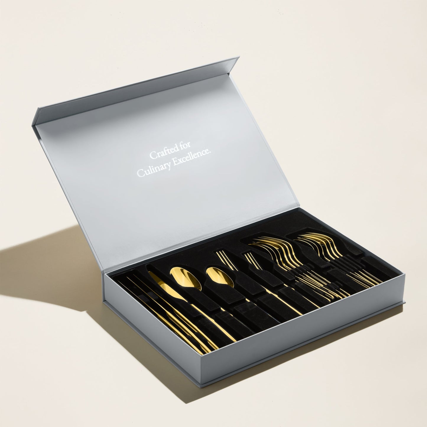 Set of gold cutlery in an open gray box on a light beige background