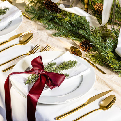 Elegant Christmas table setting with gold cutlery, white plates, and greenery.