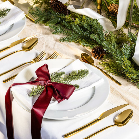 Elegant Christmas table setting with gold cutlery, white plates, and greenery.