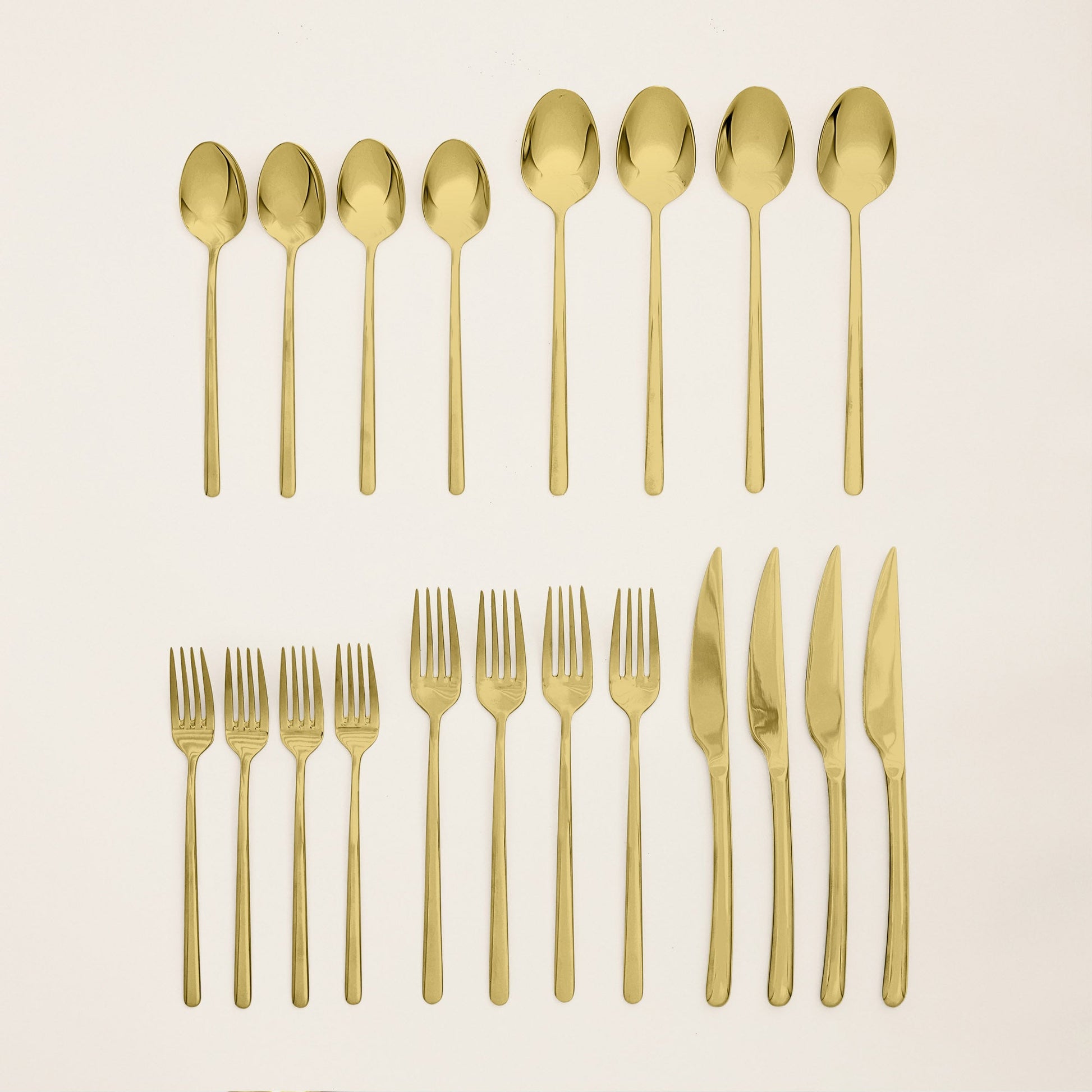Set of gold cutlery including spoons, forks, and knives on a beige background