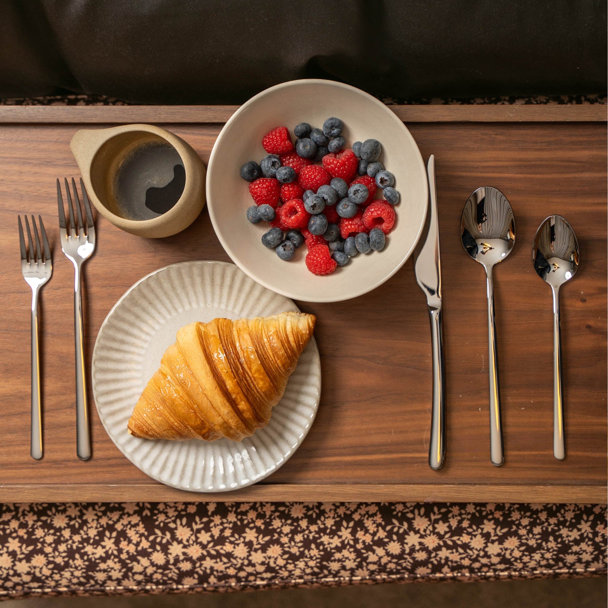Breakfast setting with croissant, berries, and utensils on a wooden table.
