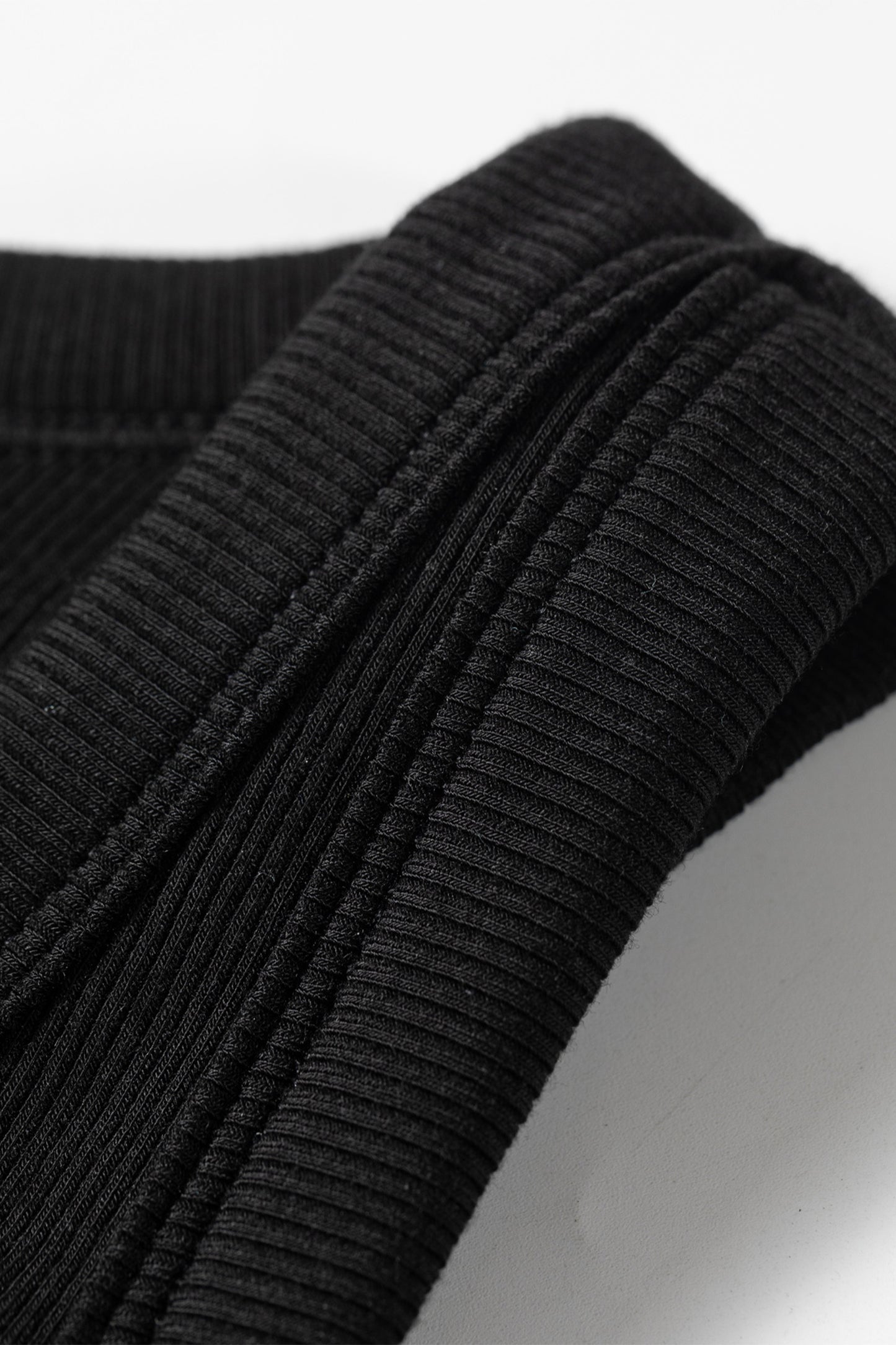 Close-up of a black ribbed sweater sleeve on a light gray background
