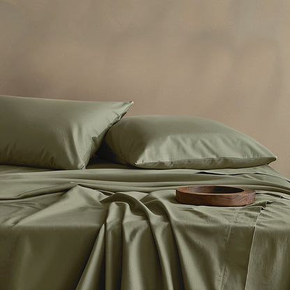 Green bed sheets and pillows on a bed with a wooden tray on a beige background