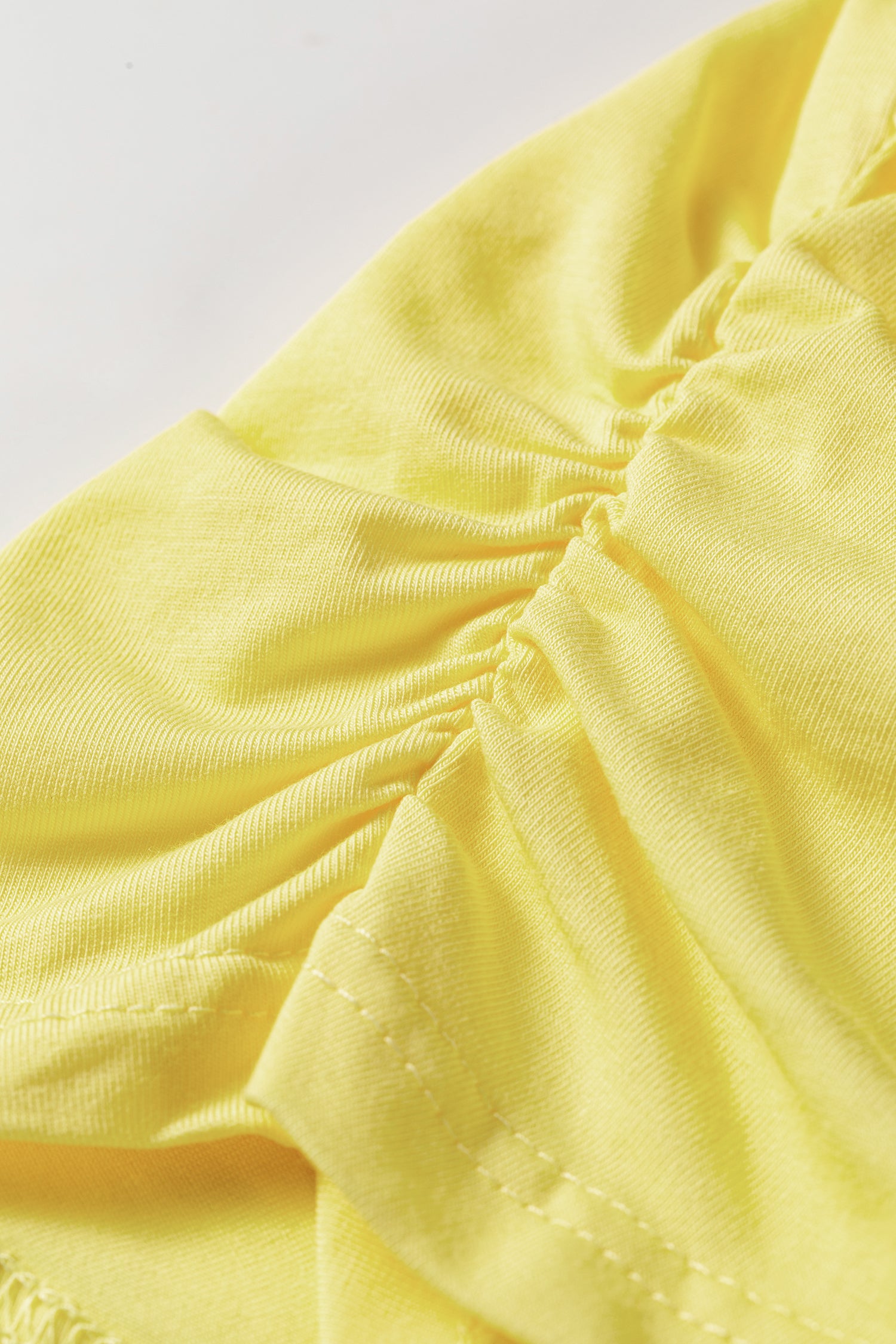 Close-up of a light yellow fabric garment with gathered ruching and visible stitching details.