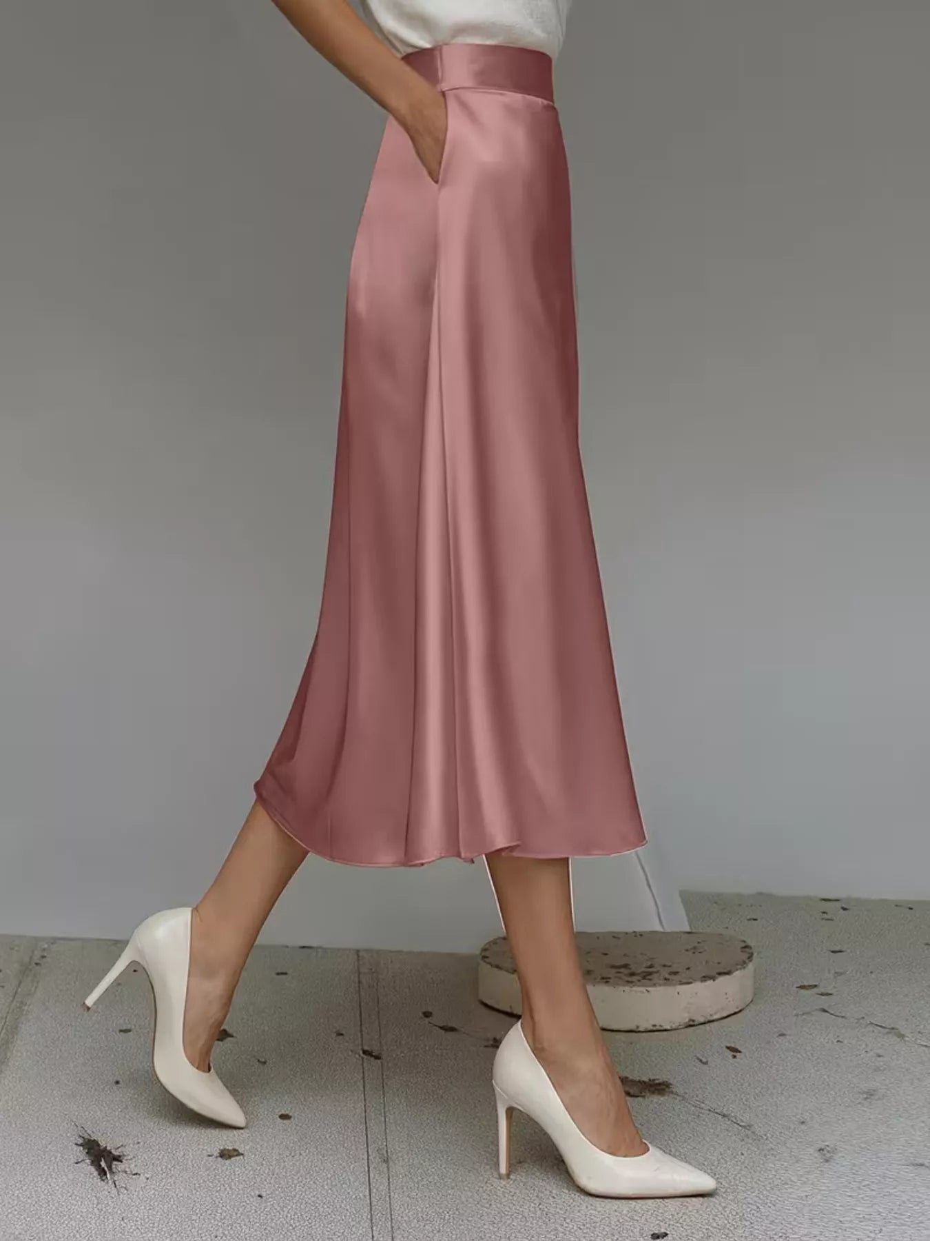 Person wearing a pink satin skirt and white high-heeled shoes on a neutral background
