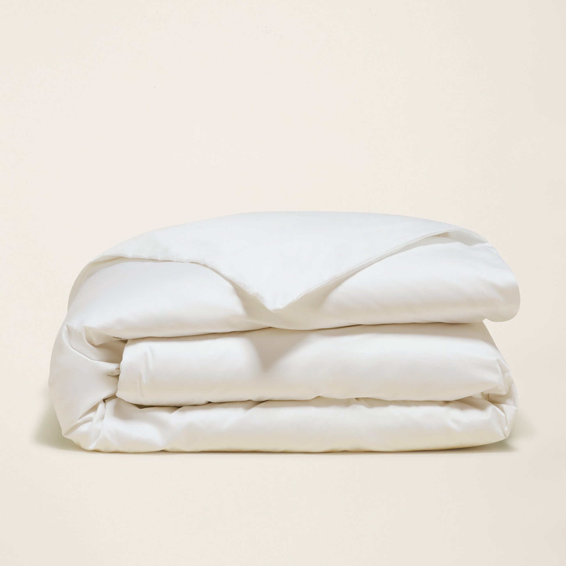 Folded white comforter on a beige background